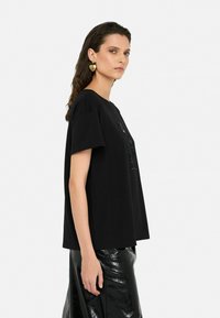 Zwarte katoenen t-shirt met korte mouwen en een relaxed fit, met een paillettenlogo op de voorkant. Gemaakt met een glanzende zwarte rok.