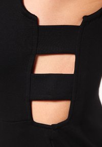 Schwarzes Stoffkleidungsstück mit Ausschnitten an der Seite, verstärkten Kanten und einer glatten, dehnbaren Textur.