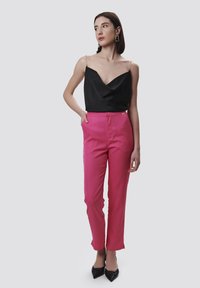 Zwarte satijnen top met een V-hals, gecombineerd met high-waisted roze broeken, die een op maat gemaakte fit en strakke textuur laten zien. Draagster in zwarte hakken.