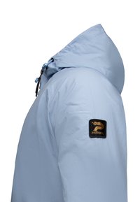 Light blue jacket with a hood, made of lightweight fabric. Features a black and gold logo patch on the left sleeve and adjustable drawstrings.