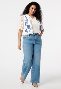 Jeans in lichtblauwe denim met een ontspannen pasvorm, gecombineerd met een crèmekleurige blouse met blauwe bloemenborduursels en kantmouwen.