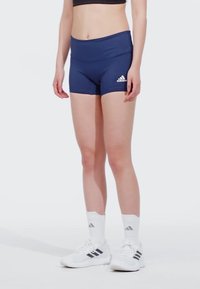 Pantaloni sportivi blu navy con vita alta e logo Adidas bianco. Indossati con calze bianche e scarpe con dettagli grigi.