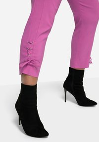 Lyserøde bukser med et tætsiddende design, der har snøredetaljer med sølvøjer i kanten, parret med sorte suede ankelstøvler.