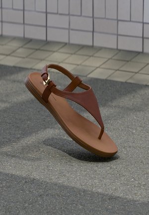 Pruun nahast sandaal kuldse pandlaga, varbapaelaga ja lameda tallaga, väljas asfaldil plaatidega seina lähedal eksponeeritud.