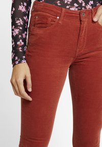 Röda kordflossbyxor med en smal passform. Har framfickor och en knappstängning vid midjan. Strukturen av det ribbade tyget är synlig.