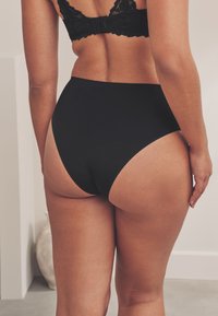 Slip nero a vita alta in tessuto liscio, con design senza cuciture e copertura minima sul retro, dalla forma pulita e sagomata.