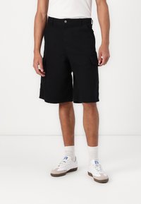 Pantaloni scurți cargo negri cu două buzunare laterale, față plată și tiv drept. Confecționați dintr-un material ușor, asortați cu adidași albi.