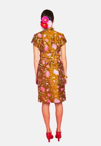 Braunfarbenes Kurzarmkleid mit lebhaften floralem Stickereien in Pink und Grün. Es hat einen taillierten Schnitt und reicht bis zur Mitte des Oberschenkels, kombiniert mit roten Absätzen.