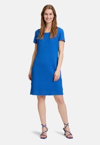 Blaues strukturiertes Kleid mit kurzärmeligen, knielangen Schnitt und gerader Silhouette. Kombiniert mit blauen Riemchensandalen.