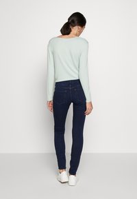 Ljusblå långärmad tröja, mörkblå figurnära jeans, vita skor; slät textur, avslappnad design, visar bakvy.