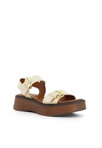 Crème leren platform sandaal met twee verstelbare banden en goudkleurige gespen. Voorzien van een robuuste bruine houten zool en een getextureerde voetbed.