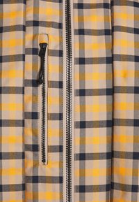 Tkanina w kratę w kolorach żółtym, szarym i granatowym; posiada zamek błyskawiczny z przodu i kieszeń boczną. Materiał wydaje się gładki i ma wyraźnie zorganizowany krój.