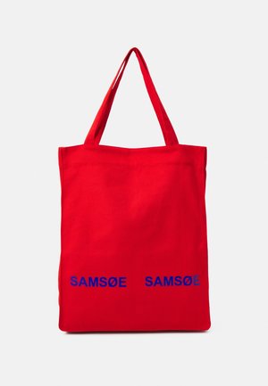 Czerwona torba materiałowa z dwoma uchwytami i niebieskim napisem „SAMSØE SAMSØE” nadrukowanym w pobliżu dolnego środka.