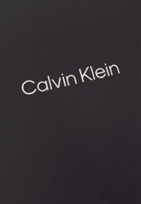 Tissu noir avec le texte blanc « Calvin Klein » imprimé en police simple et moderne, centré sur la surface.