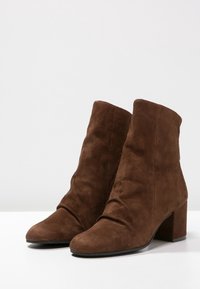 Braune Wildleder-Stiefeletten mit einem lässigen Design, spitzen Zehen und einem klobigen Absatz. Glatte Textur mit einer einfachen und klaren Silhouette.