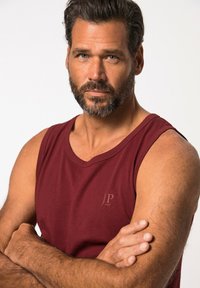 Burgundy sleeveless tank top in soft fabric with a crew neckline and a small, embossed logo on the left chest area.