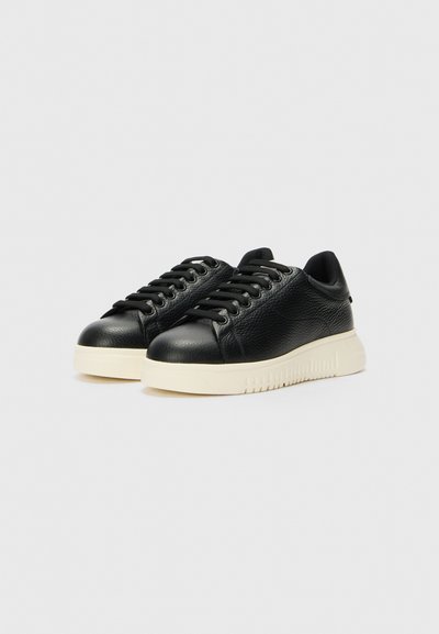 Svarta lädersneakers med texturerad ovandel, rund tå och kontrasterande beige gummisula. Har svarta snörningar och en minimalistisk design.