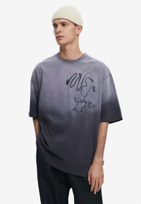 Camiseta de gran tamaño con degradado de p�úrpura a negro, mangas cortas y texto gráfico en tinta oscura. Gorro de punto cálido y texturizado.
