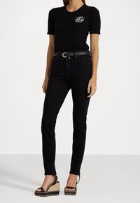 Svart kortärmad stickad topp med broderad logotyp, tillsammans med högmidjade svarta jeans och svarta kilklackar med vävd sula.