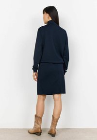 Navy blue two-piece outfit consisting of a long-sleeve top with a high collar and a knee-length skirt, paired with light brown ankle boots.