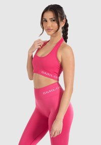 Sujetador deportivo rosa y leggins de tiro alto a juego. Textura acanalada con el nombre de la marca "SMILODON" en blanco a lo largo de la cinturilla y la banda del sujetador.