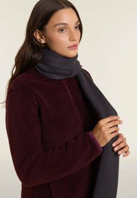 Sciarpa a coste grigia scura drappeggiata attorno al collo, in contrasto con la giacca in fleece bordeaux. Texture liscia e design caldo.