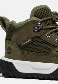 Chaussures de randonnée vertes avec un design en suède et en maille, dotées d'un col rembourré, de lacets ajustables et d'une semelle extérieure en caoutchouc noir avec des motifs de traction.