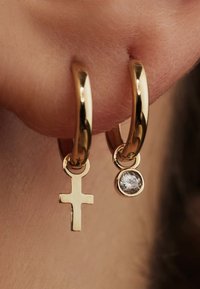 Gold hoop earrings feature a small cross charm and a single clear gemstone, showcasing a polished finish and smooth texture.
