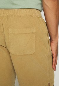 Shorts en velours côtelé marron avec une ceinture élastique, dotés d'une poche arrière plaquée et de bords effilochés pour un ajustement décontracté.