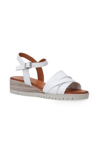 Witte leren wedge sandalen met een kruislings ontwerp aan de voorkant, verstelbare enkelsluiting en een gestructureerde middelhoge hak. Donkere binnenzool.