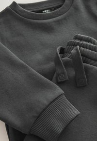 Dunkelgrauer Hoodie mit geripptem Rundhals- und Bündchen; passende Jogginghose mit elastischem Bund und zwei aufgenähten Kordelzügen. Weicher Stoff mit angenehmem Griff.
