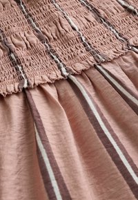 Lähivõte roosast kangast, millel on vertikaalsed pruunid ja valged triibud, varustatud kogutud elastse smockinguga ja volangidega servade detailidega.