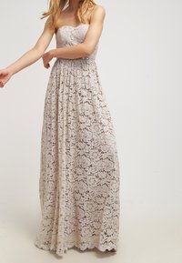 Strapless maxi dress in cream lace, featuring floral patterns, a fitted bodice, and a flowing skirt with a scalloped hem.