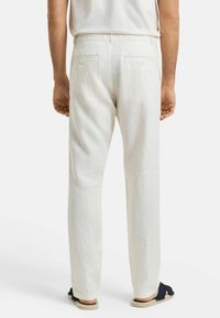 Witte linnen broek met een relaxte pasvorm, voorzien van achterzakken en een gladde textuur. Gekocht met donkere sandalen.