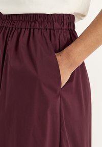Bordeauxrok met een elastische tailleband, zijzakken en zachte, lichtgewicht stof. Eenvoudig ontwerp zonder zichtbare patronen.
