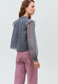 Blusa trasparente a fantasia nei toni del blu e del viola con dettagli arricciati; abbinata a pantaloni rosa con applicazioni a forma di stella sulle tasche.