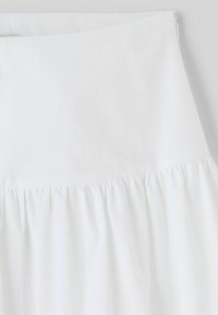 Jupe blanche en tissu léger avec taille froncée. Présente un haut lisse avec des plis en bas et une fermeture éclair dissimulée.