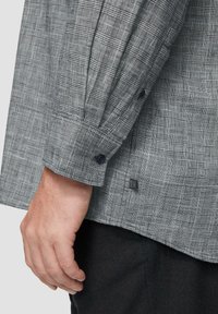 Grijs geruit overhemd met lange mouwen en een knoopmanchet. Heeft een textuurstof met een subtiele ruitpatroon en fijne stikdetails.