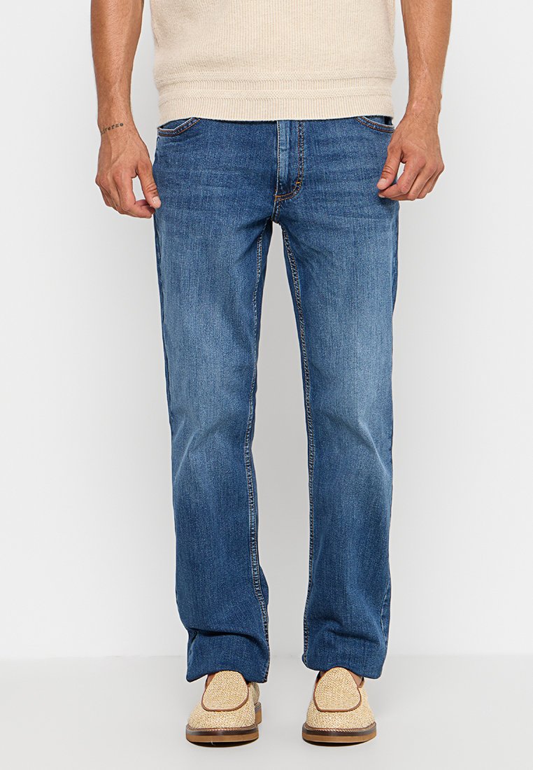 Jasnoniebieskie dżinsy o prostym kroju, z pięcioma kieszeniami i kontrastowym przeszyciem, zestawione z beżowymi butami i jasnym swetrem.