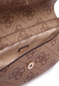 Interno della borsa a tracolla con motivo marrone, caratterizzato da un tessuto testurizzato, chiusura a scatto e una fodera in raso con il marchio "GUESS" ripetuto.