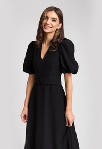 Czarna sukienka z bufkami, dekoltem w serek i dopasowanym pasem. Wykonana z gładkiego materiału z lekko opadającą spódnicą.