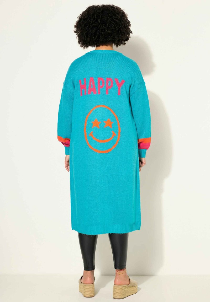 Türkiser langer Cardigan mit "HAPPY" in Pink und einem Smiley-Gesicht-Design in Orange. Bietet bunte gestreifte Ärmel und einen gerippten Saum.
