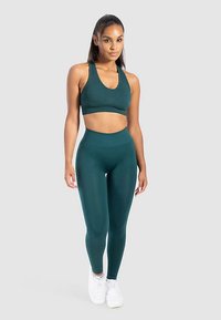 Reggiseno sportivo turchese e leggings a vita alta abbinati realizzati in un tessuto elastico e testurizzato. Scarpe da ginnastica bianche completano l'abbigliamento sportivo.