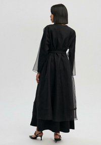 Must maxi kleit läbipaistvate pikkade varrukatega, vöökohal vöö ja voolava äärega. Siidine kangas tekstuurse pealiskihiga. Madala kontsaga rihmikud sandaalid.