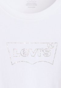 White cotton t-shirt featuring a Levi’s logo outlined in shimmering rhinestones, round neckline, and short sleeves.