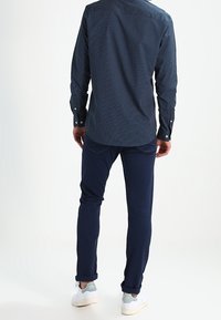 Navy patterned shirt with long sleeves and buttoned cuffs, paired with dark navy trousers and white sneakers. Back view showcased.