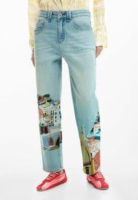 Blugi din denim albastru deschis cu un decor vibrant pictat reprezentând clădiri de coastă pe picioare. Croială dreaptă cu o potrivire ușor lejeră, asortați cu pantofi roșii.