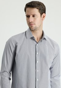 Camisa de botones a rayas en azul claro y blanco. Presenta un cuello extendido, mangas largas y una textura tejida suave. Siete botones en la parte frontal.