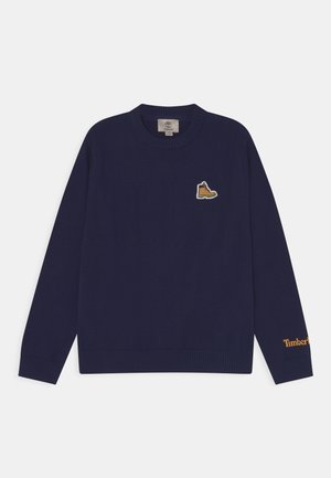Suéter de punto azul marino con mangas largas, puños y dobladillo acanalados, con un parche con el logo de una bota amarilla en el pecho y "Timberland" en naranja.