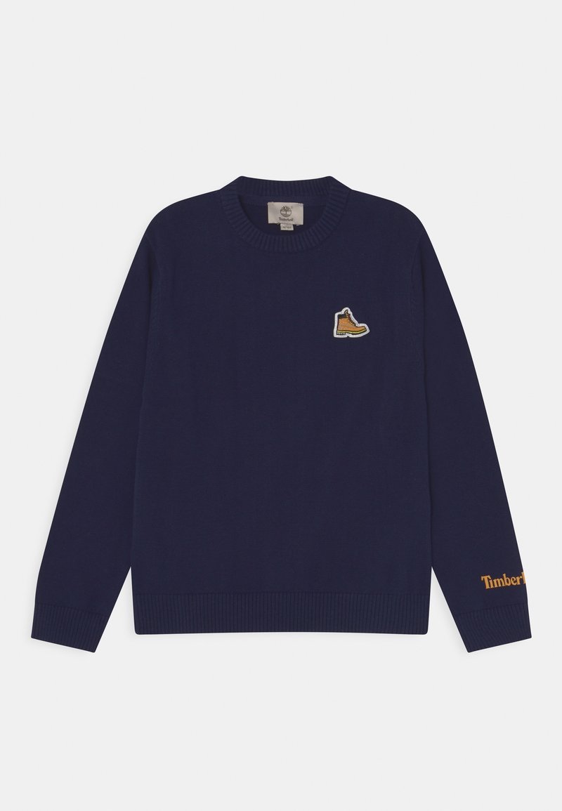Pull en maille bleu marine à manches longues, poignets et ourlet côtelés, avec un patch logo bottine jaune sur la poitrine et "Timberland" en orange.